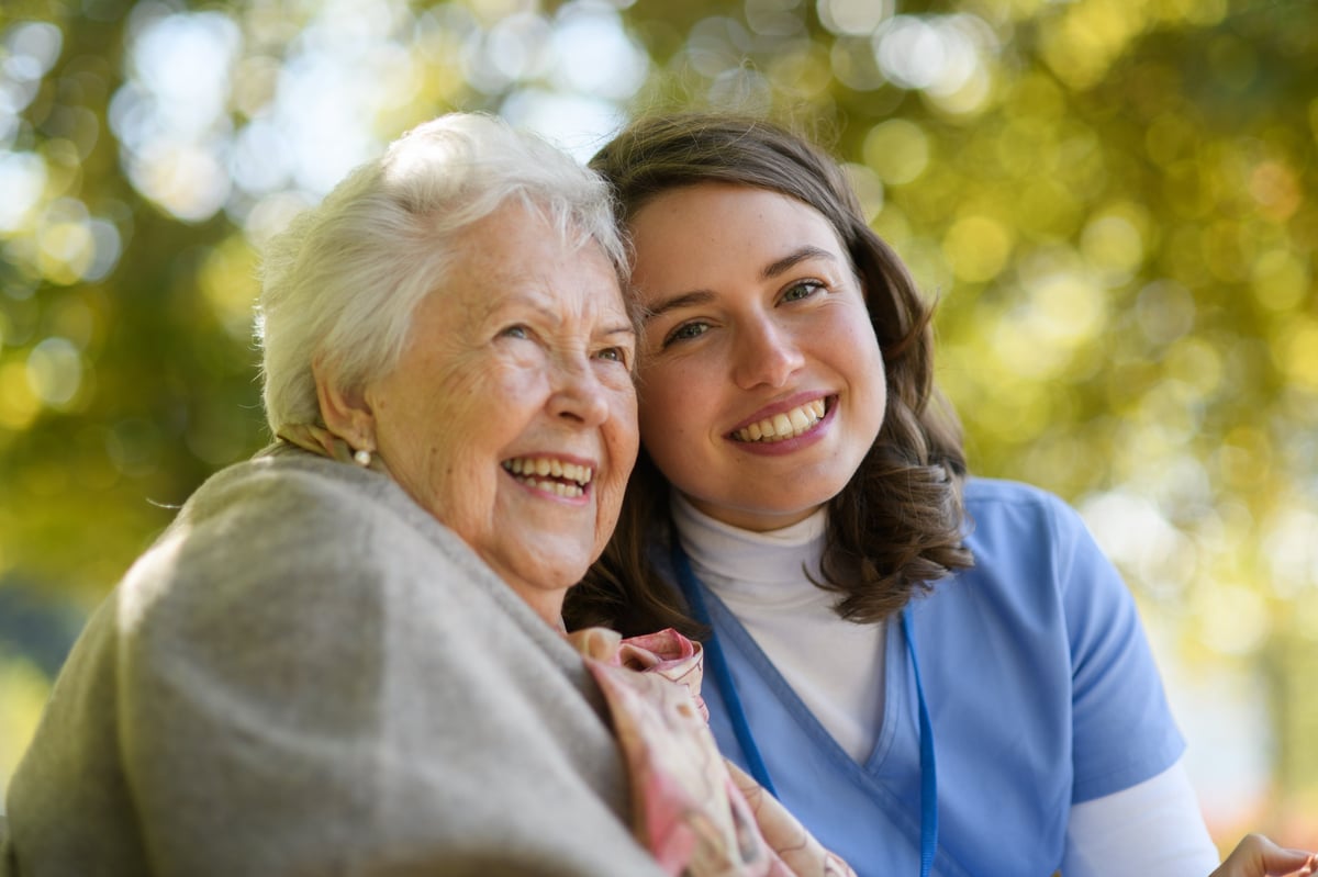 A caregiver walking outdoors with an elderly resident on a warm autumn day