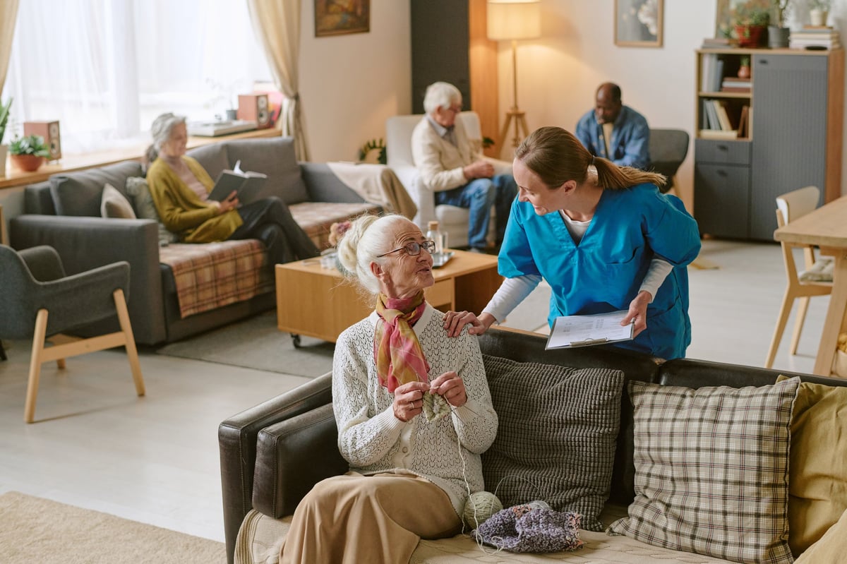 A caregiver sitting with a resident, sharing progress on her crocheting